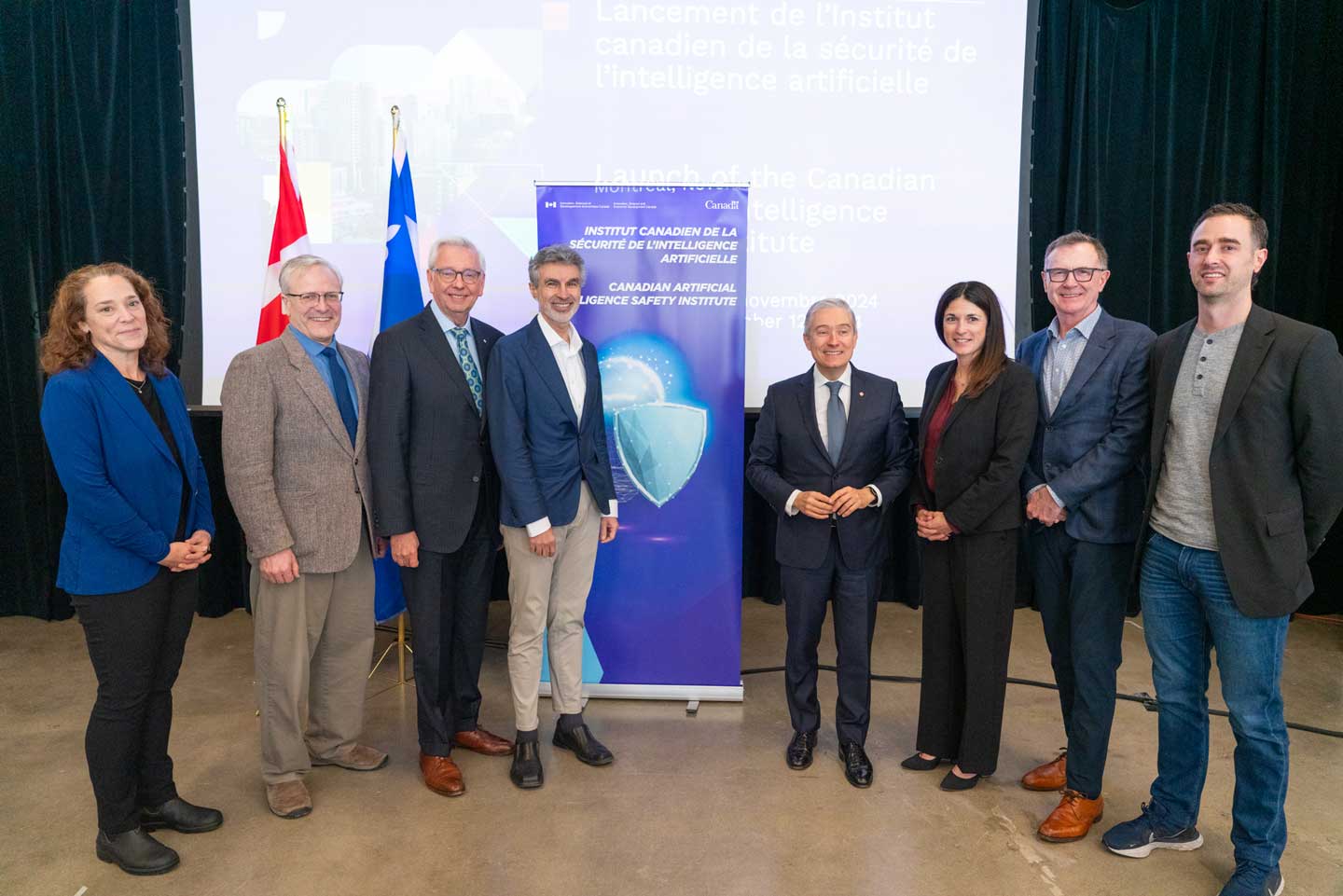 Un groupe de personnes se tient à côté d'une bannière de la CAISI et des drapeaux canadien et québécois.